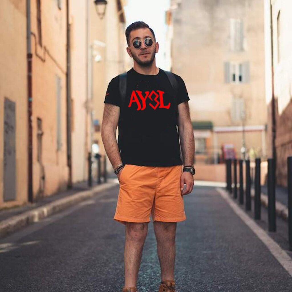 DJ AY3L portant un t-shirt noir avec le logo AY3L rouge dans une rue urbaine
