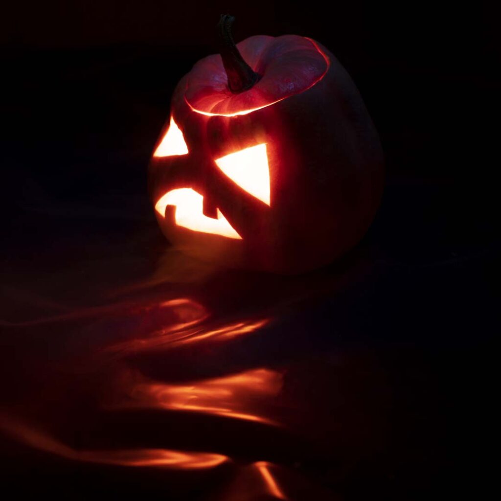 Citrouille d’Halloween sculptée, éclairée de l’intérieur, posée dans l’obscurité avec reflets orange au sol