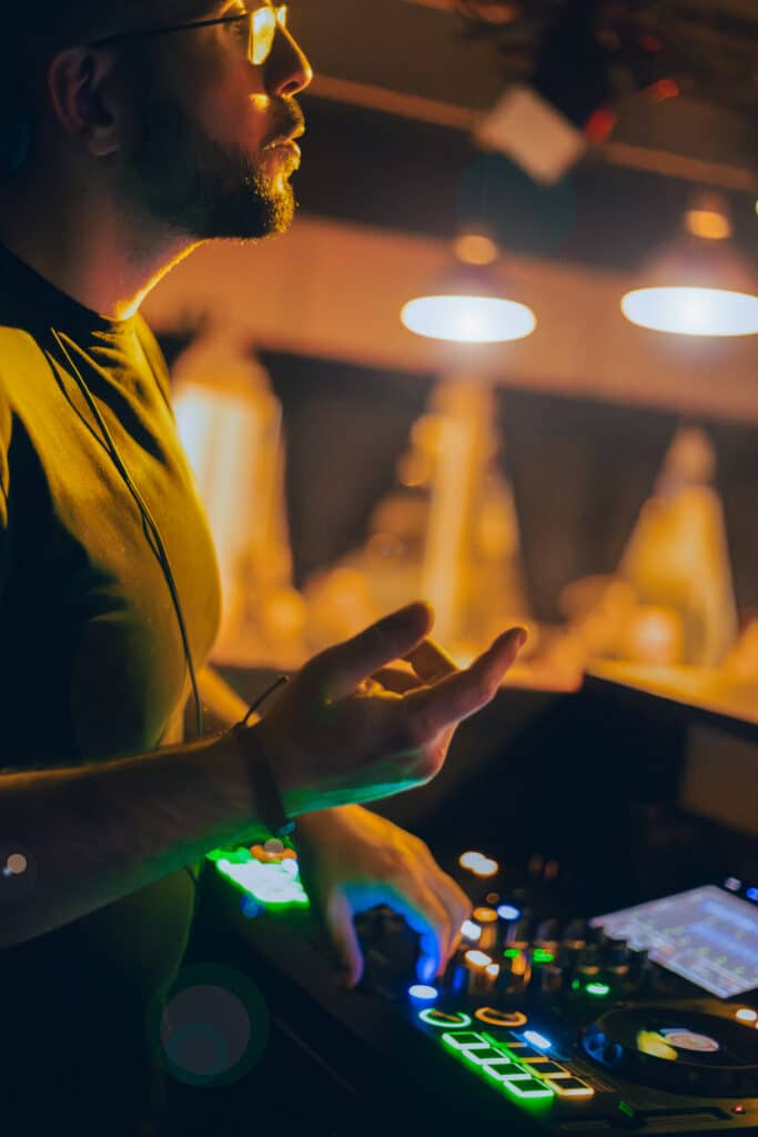 DJ AY3L mixe dans un bar avec une ambiance lumineuse chaude et le public en arrière-plan