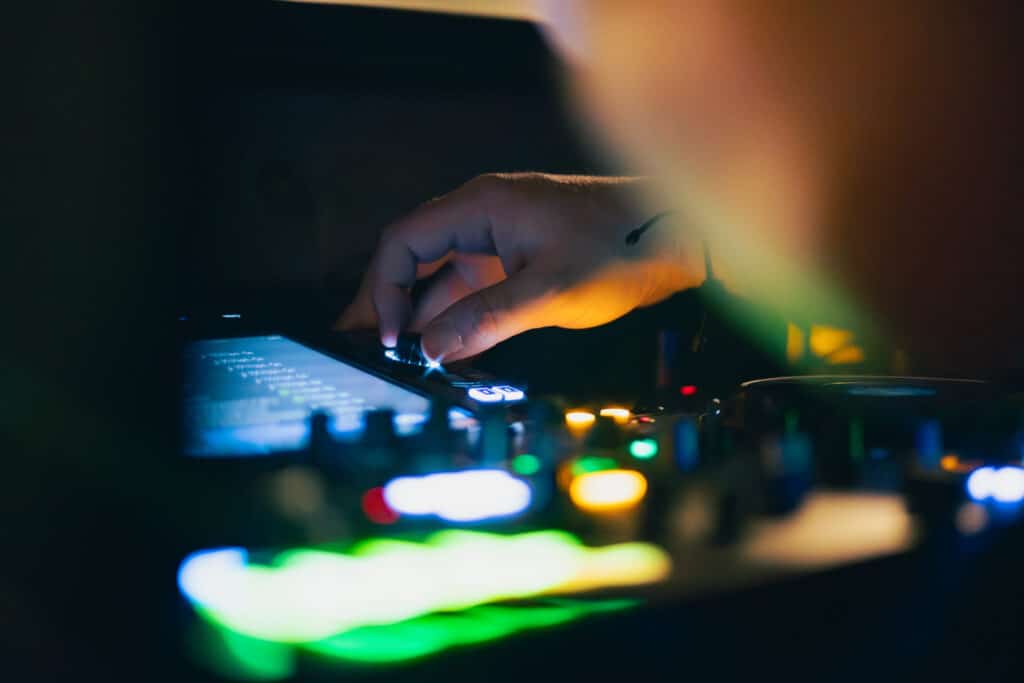 Main de DJ AY3L réglant une platine DJ avec des lumières colorées