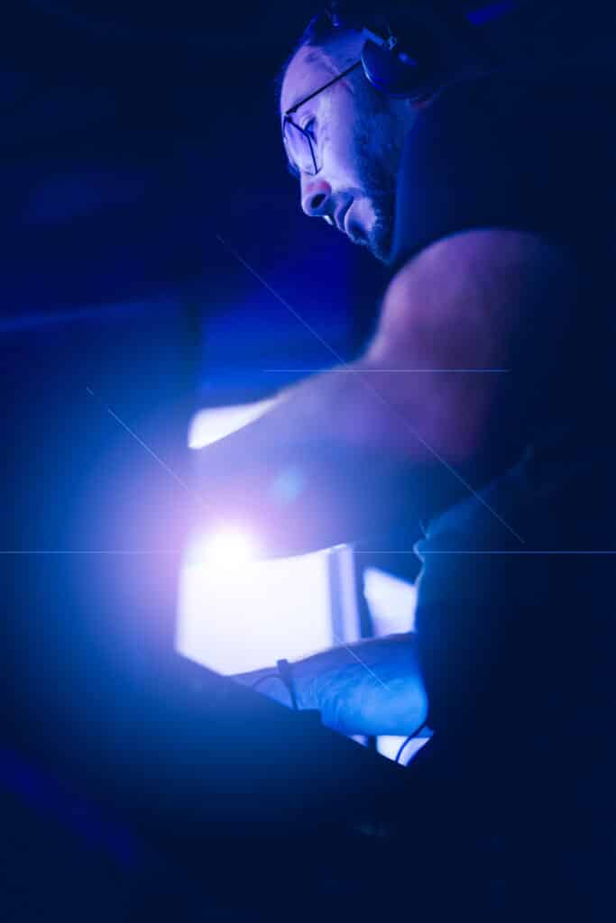 Portrait de DJ AY3L concentré sur ses platines sous une lumière bleue