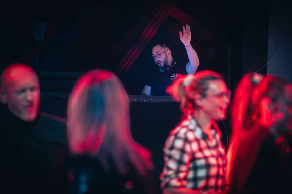 DJ AY3L lève la main derrière les platines pendant une soirée avec le public au premier plan