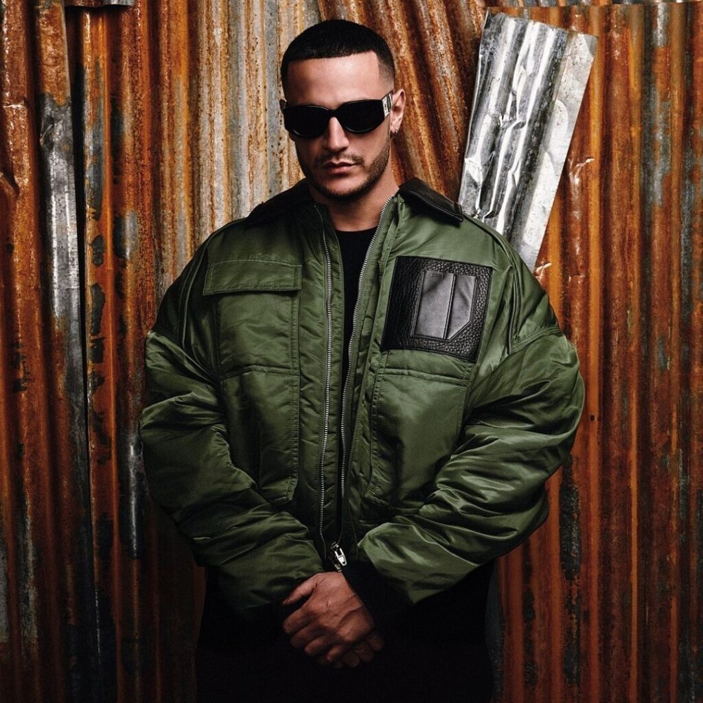 Portrait de DJ Snake en blouson vert devant une tôle rouillée, utilisé pour illustrer le show Pardon My French à Lyon.
