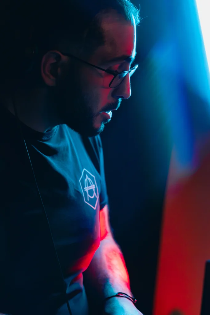 Portrait de DJ AY3L en performance, ambiance club avec éclairage bleu et rouge.