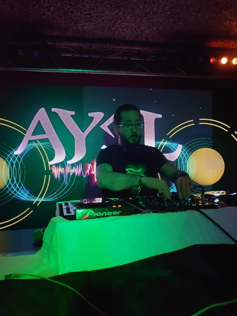 DJ AY3L mixant sur scène devant un écran lumineux affichant son logo