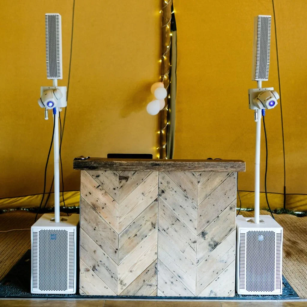 Deux enceintes colonnes blanches installées de chaque côté d'une régie DJ en bois rustique sous une tente.